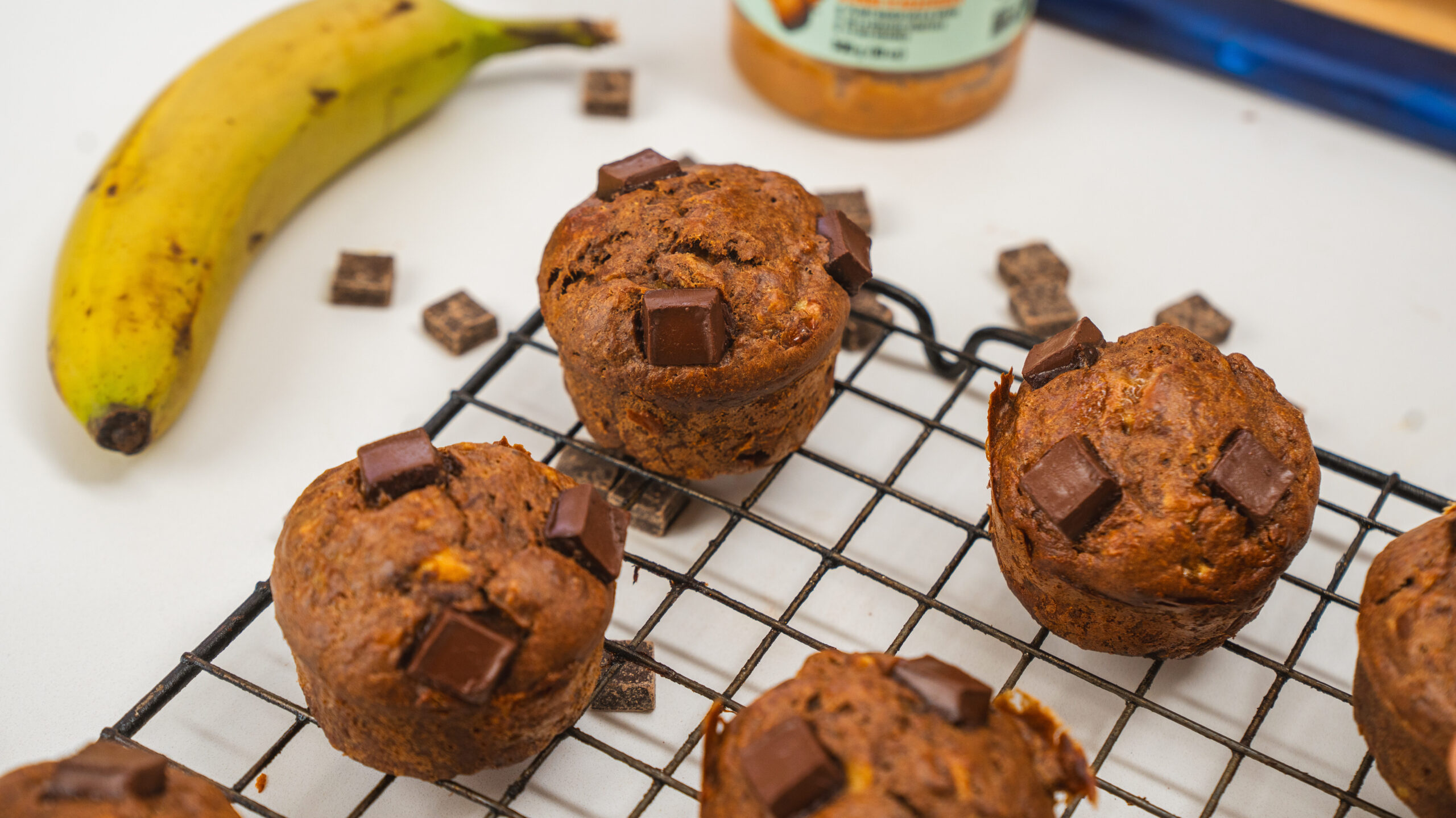 Peanut butter banana muffins with chocolate chunks on top, sitting in a wire rack