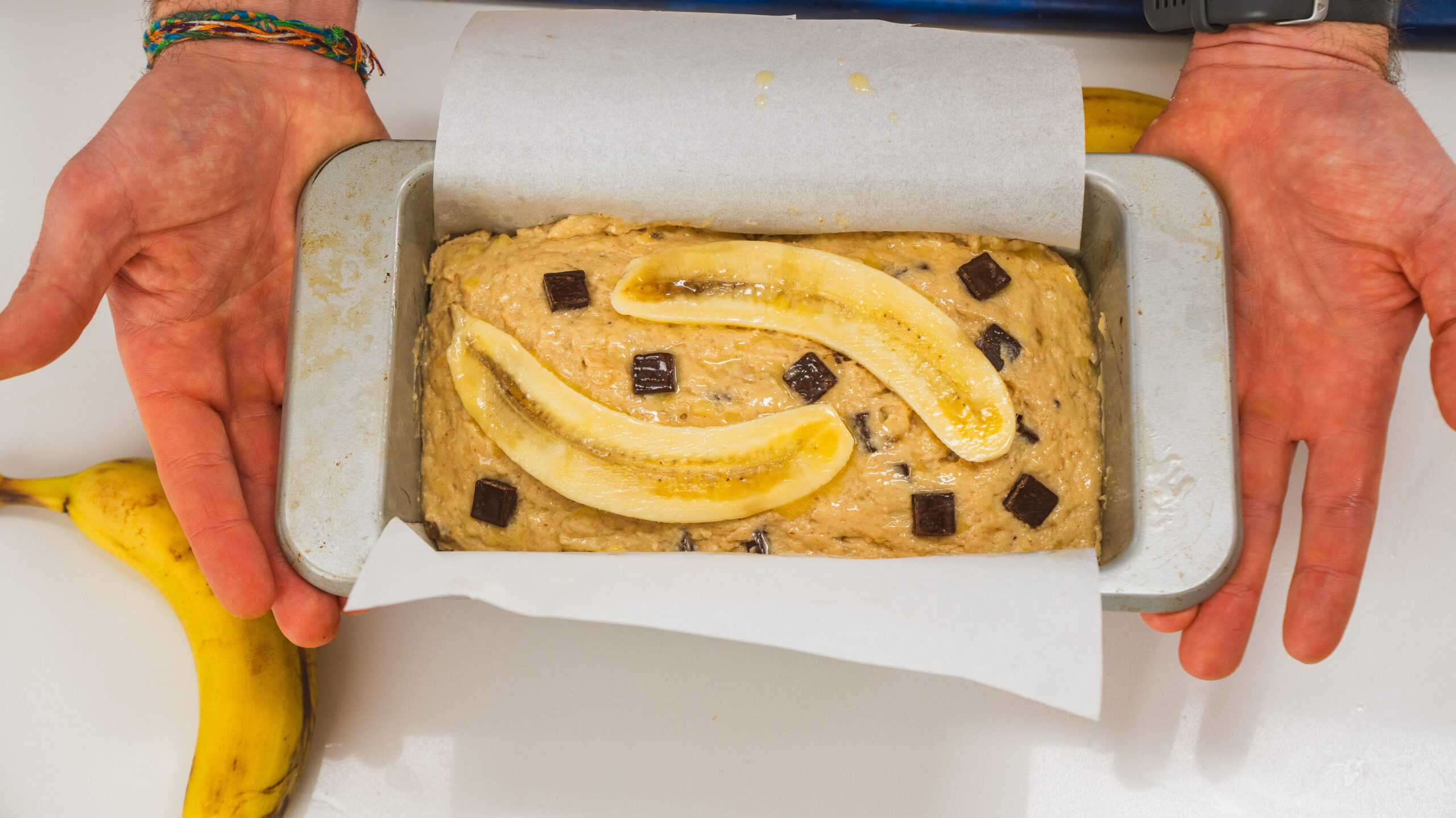 Cottage cheese banana bread batter in a loaf pan with chocolate chunks and banana slices on top.