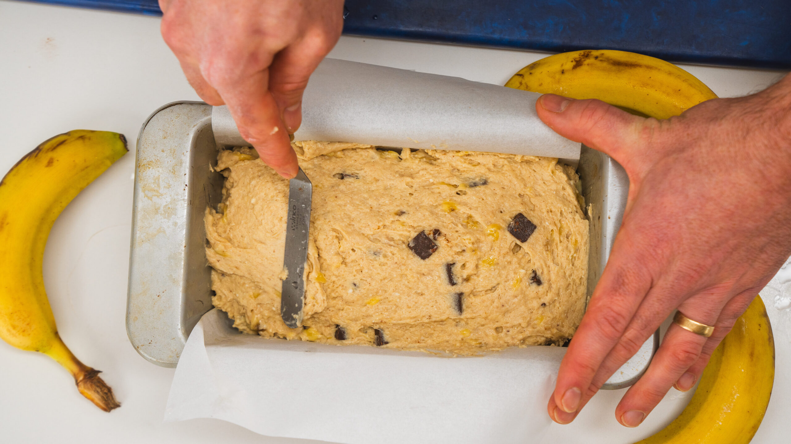 Cottage cheese banana bread batter in a parchment-lined loaf pan with a knife smoothing out the top.