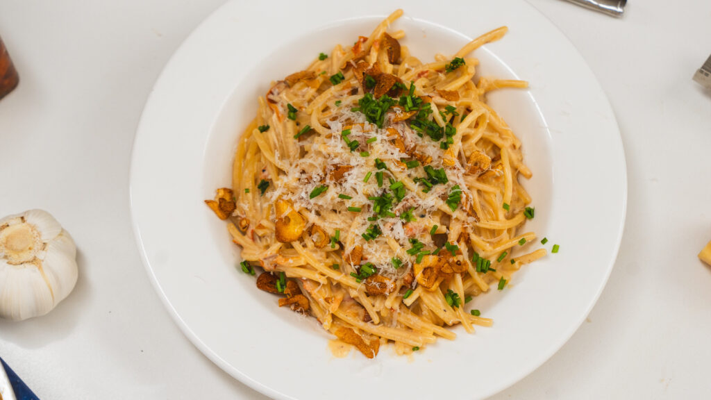 Sun dried tomato pasta in a white bowl sitting on a counter. Visible to the side is a fork and dry spaghetti.