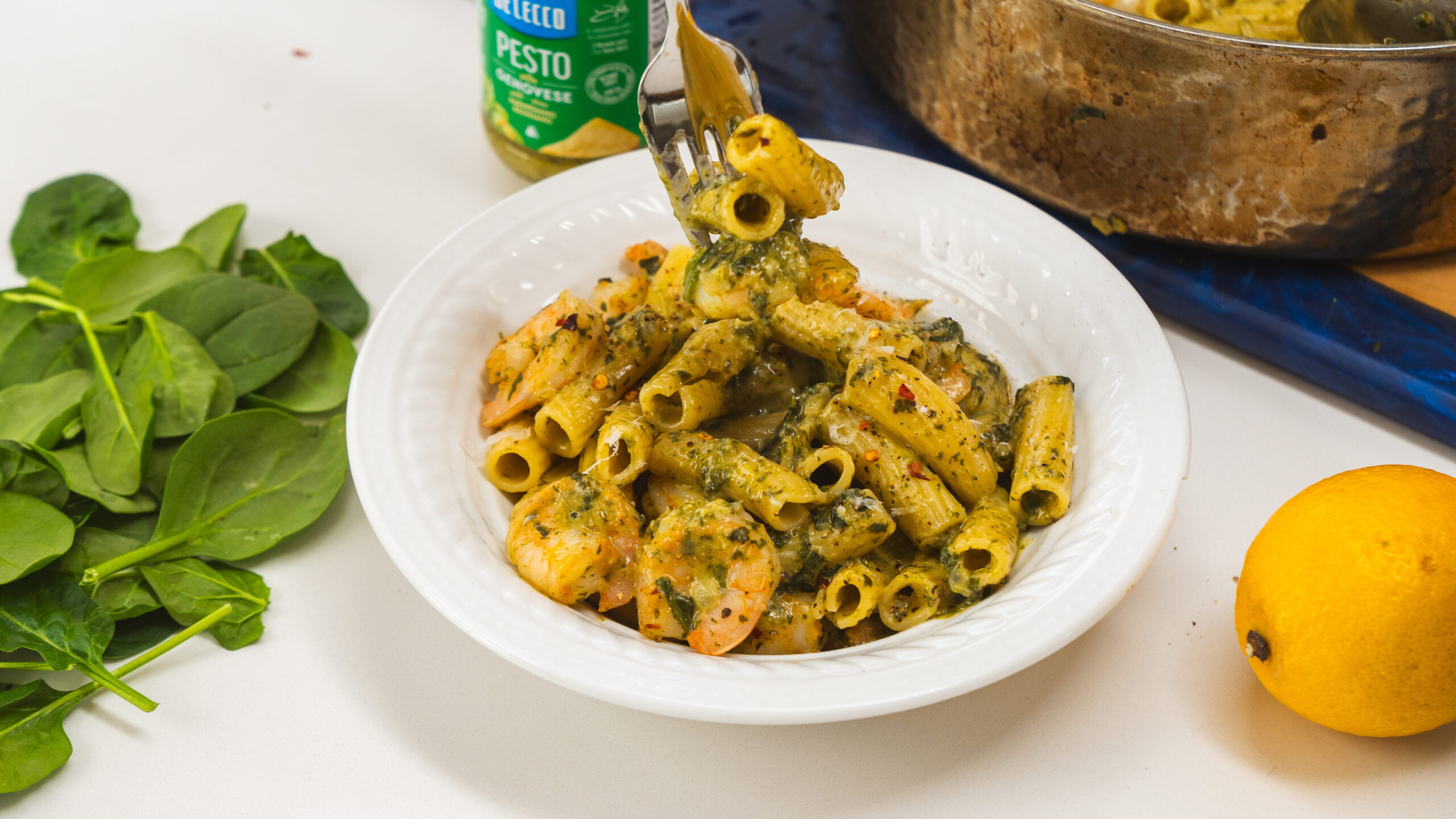 A white bowl filled with pasta and shrimp, and a fork taking some out of the bowl.