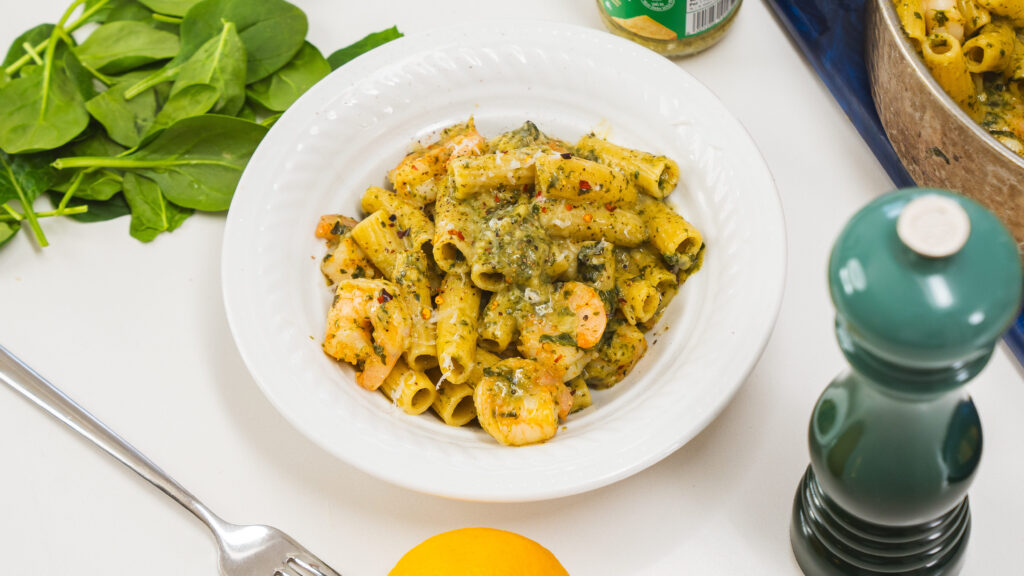 A Marry Me Pasta Recipe in a white sitting on a counter. Fresh lemon, spinach and a jar of pesto is visible to the side.