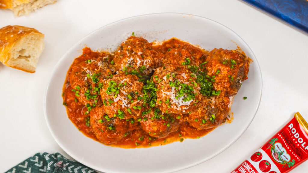 Meatballs and tomato sauce in a white bowl, topped with grated cheese. This homemade meatball recipe is bursting with flavor.