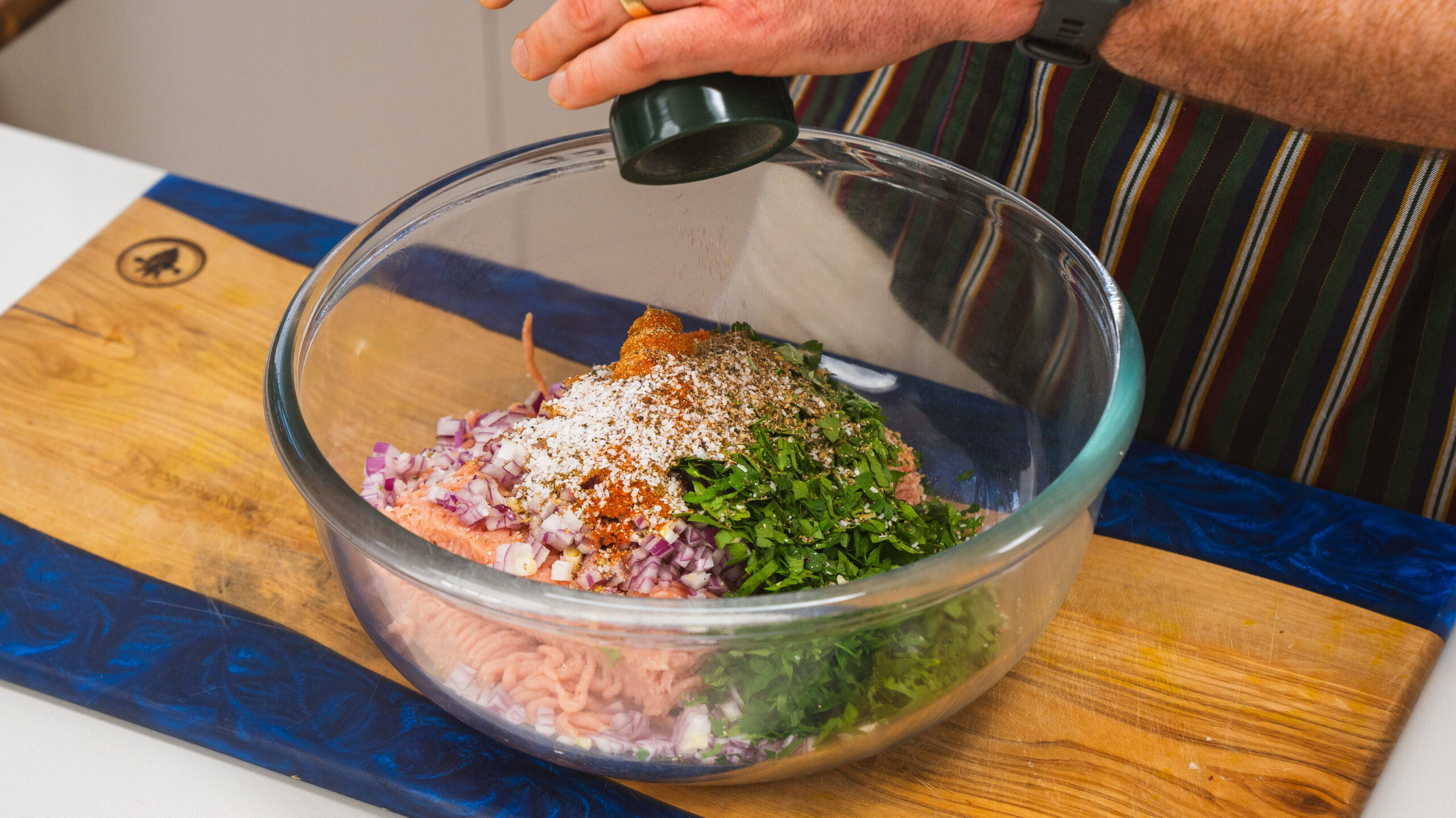 A bowl of ground chicken, onion, herbs and spices sitting on a. wooden countertop.