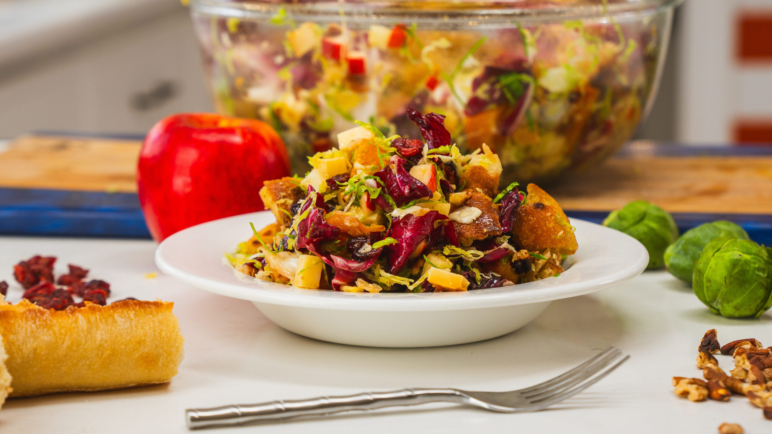 A winter panzanella salad in a white bowl sitting on a counter top. A fork is visible to the side.