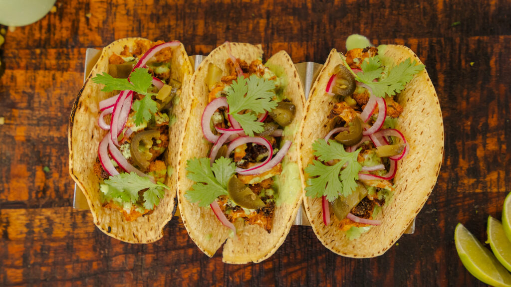 Cauliflower tacos on a wooden tray with herbs and spices on top.