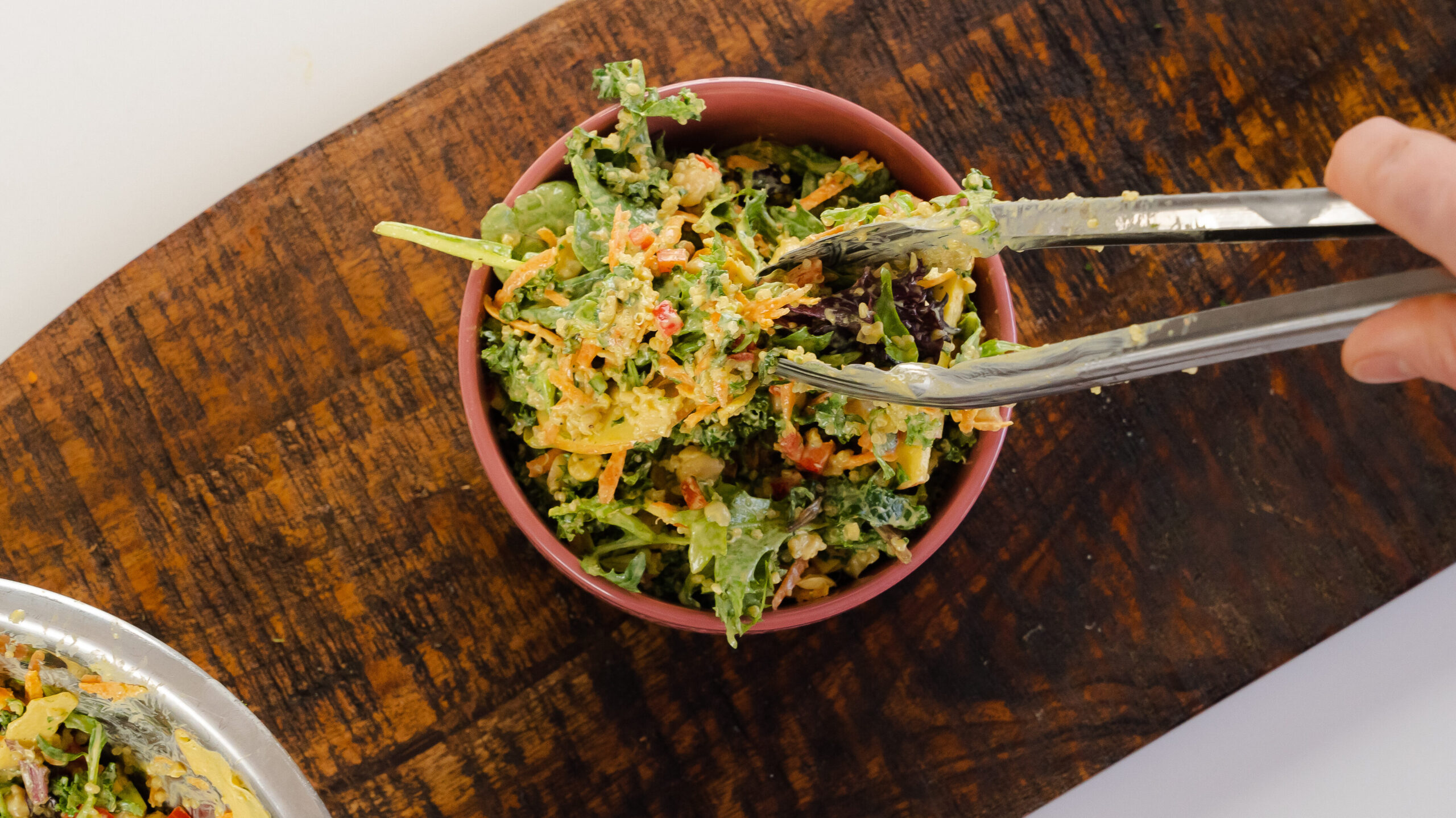 A bowl of kale quinoa salad with a pair of tongs taking some out of the bowl.