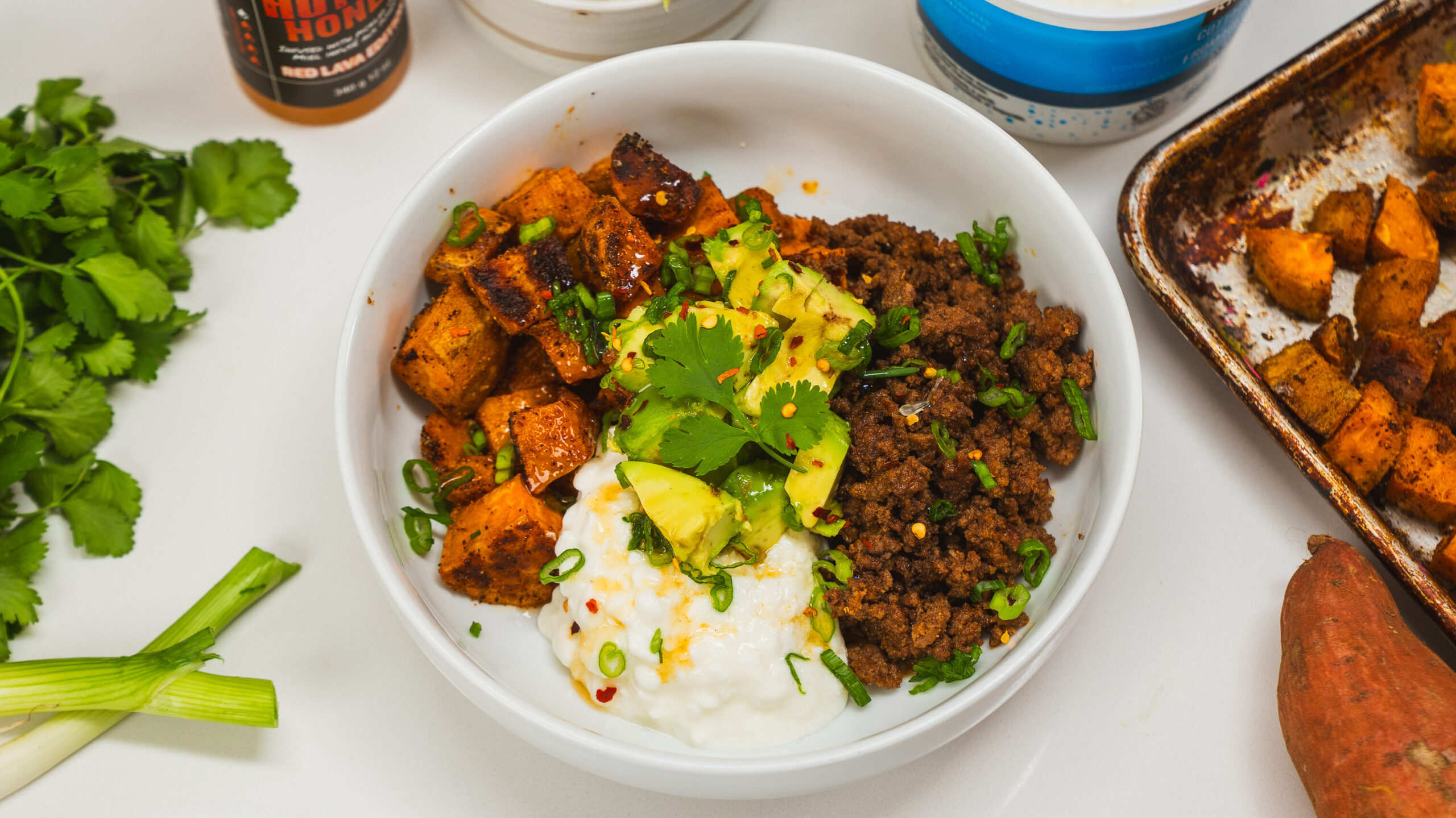 Ground beef protein bowl topped with sweet potato, cottage cheese, avocado and hot honey.