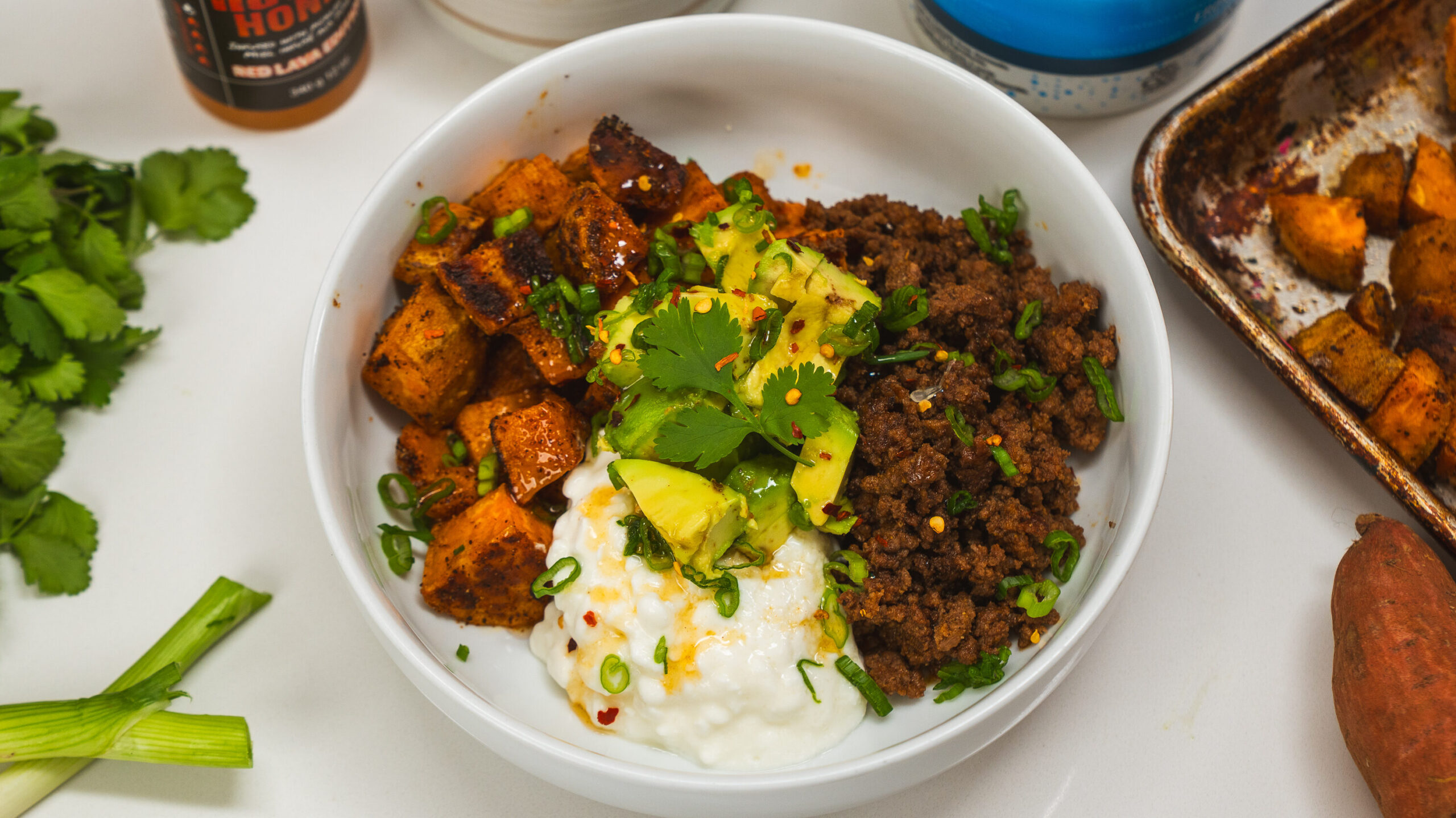 Ground beef protein bowl topped with sweet potato, cottage cheese, avocado and hot honey.