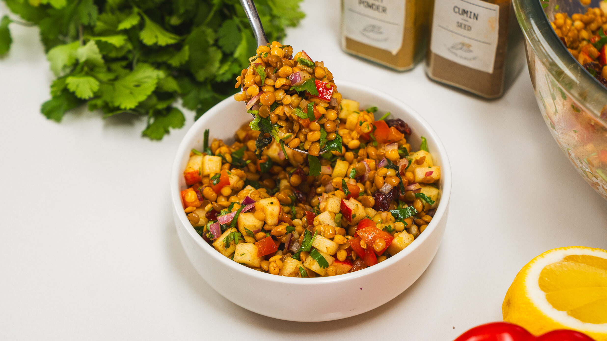 Lentil salad with herbs and spices in a white bowl with a spoon visible nearby.