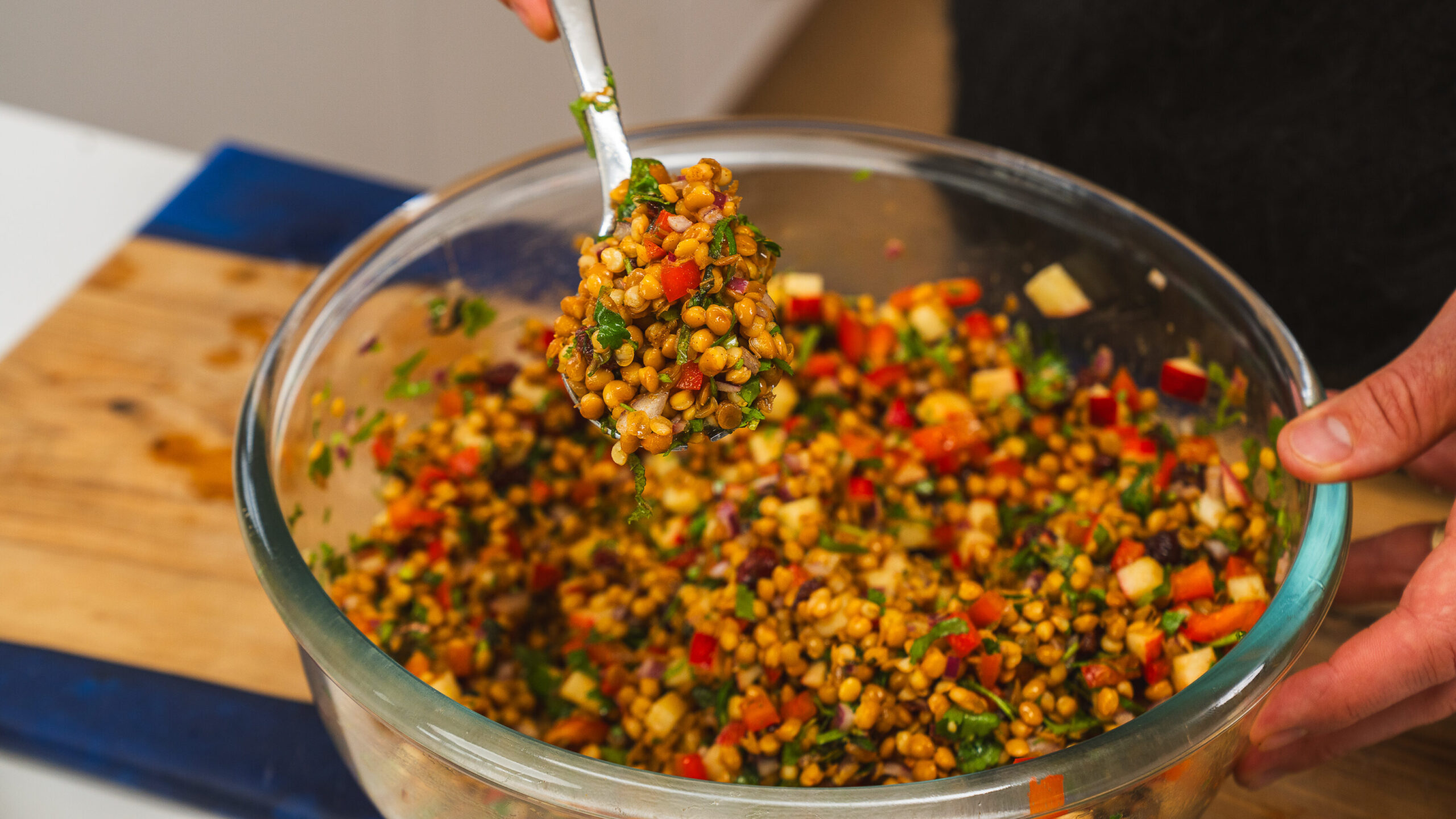 Lentil salad with herbs and spices in a clear bowl with a spoon taking a scoop out.