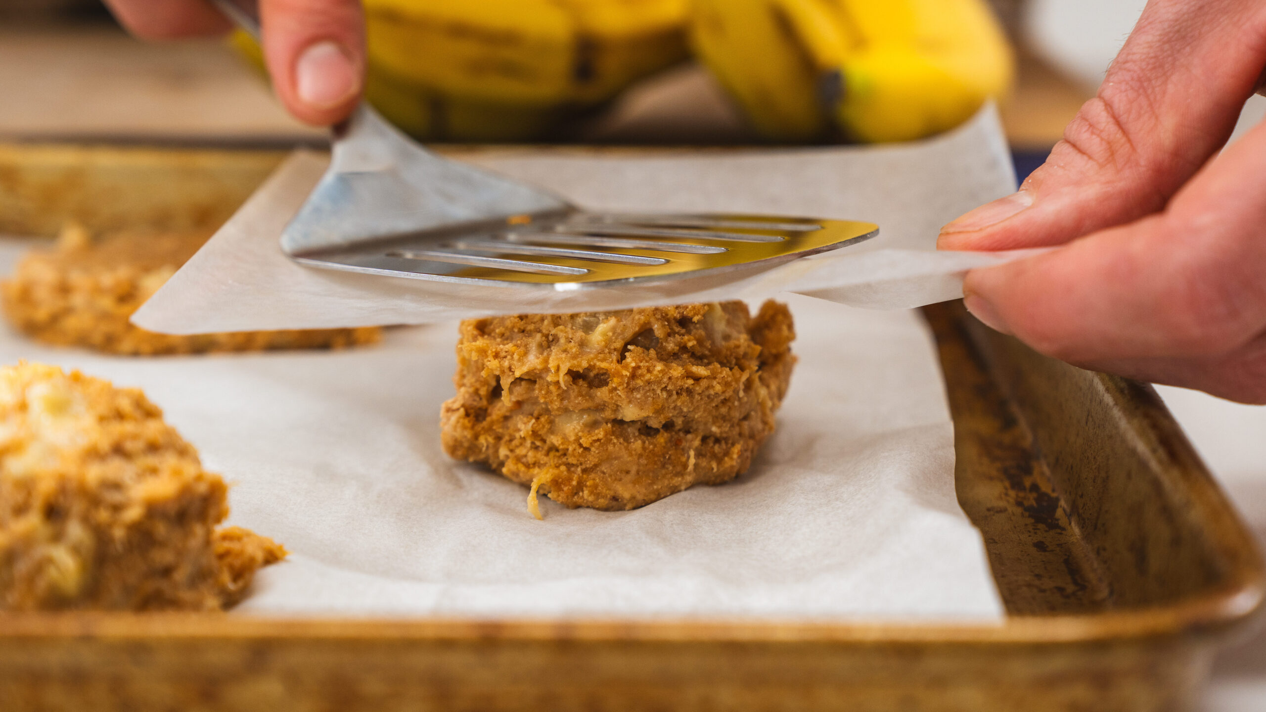 Protein chocolate chip cookies being flattened with a spatula on a cookie sheet.