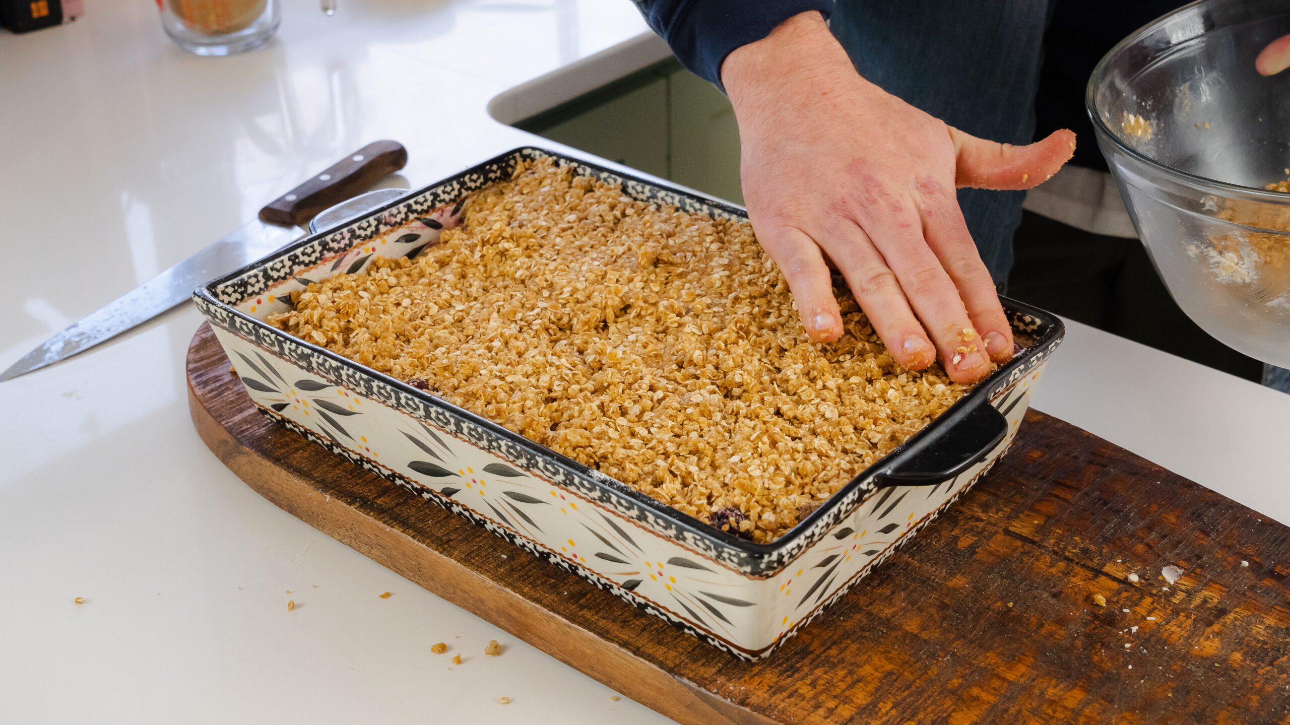 Berry crisp in a casserole pan with an oat mixture being patted down on top.