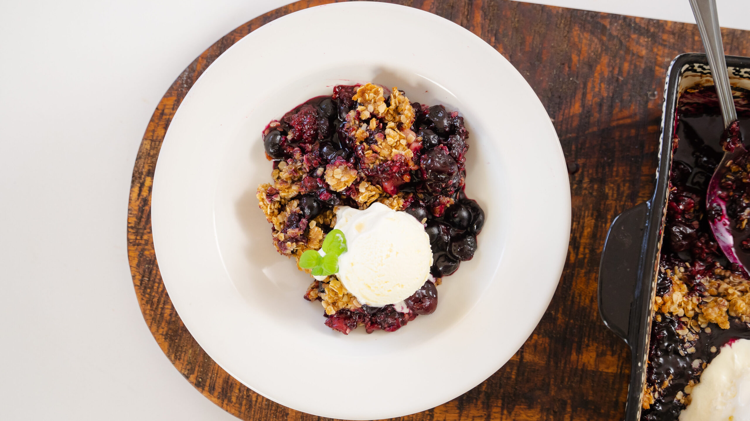 Berry crisp in a white bowl with vanilla ice cream on top.