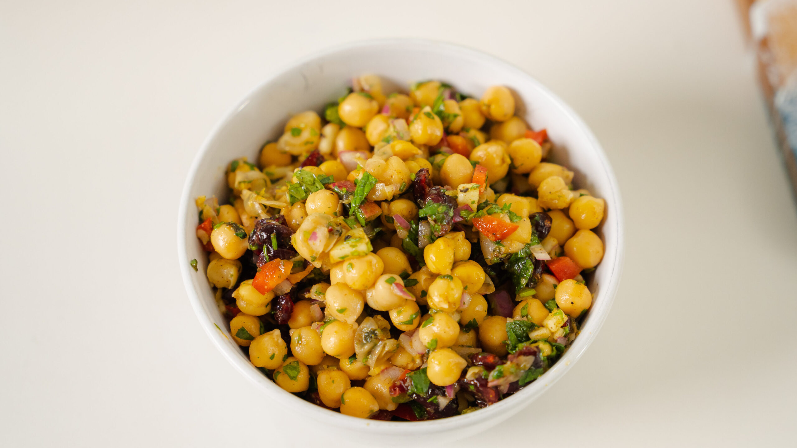 A chickpea salad with colourful veggies and fruit in a white bowl on a counter.