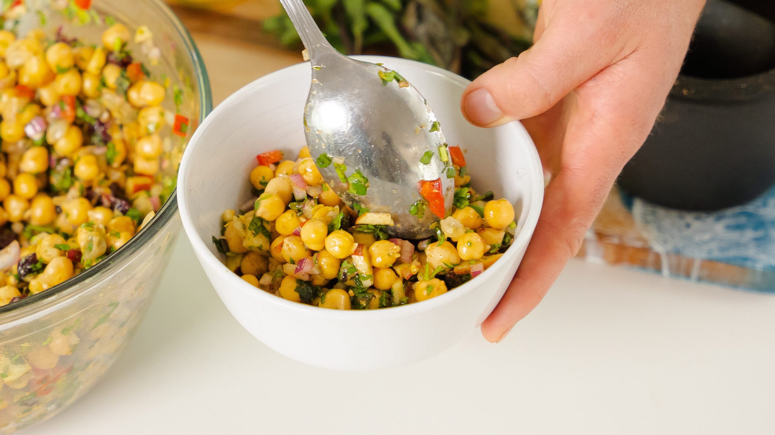 A delicious chickpea salad in a white bowl with veggies and fruit.