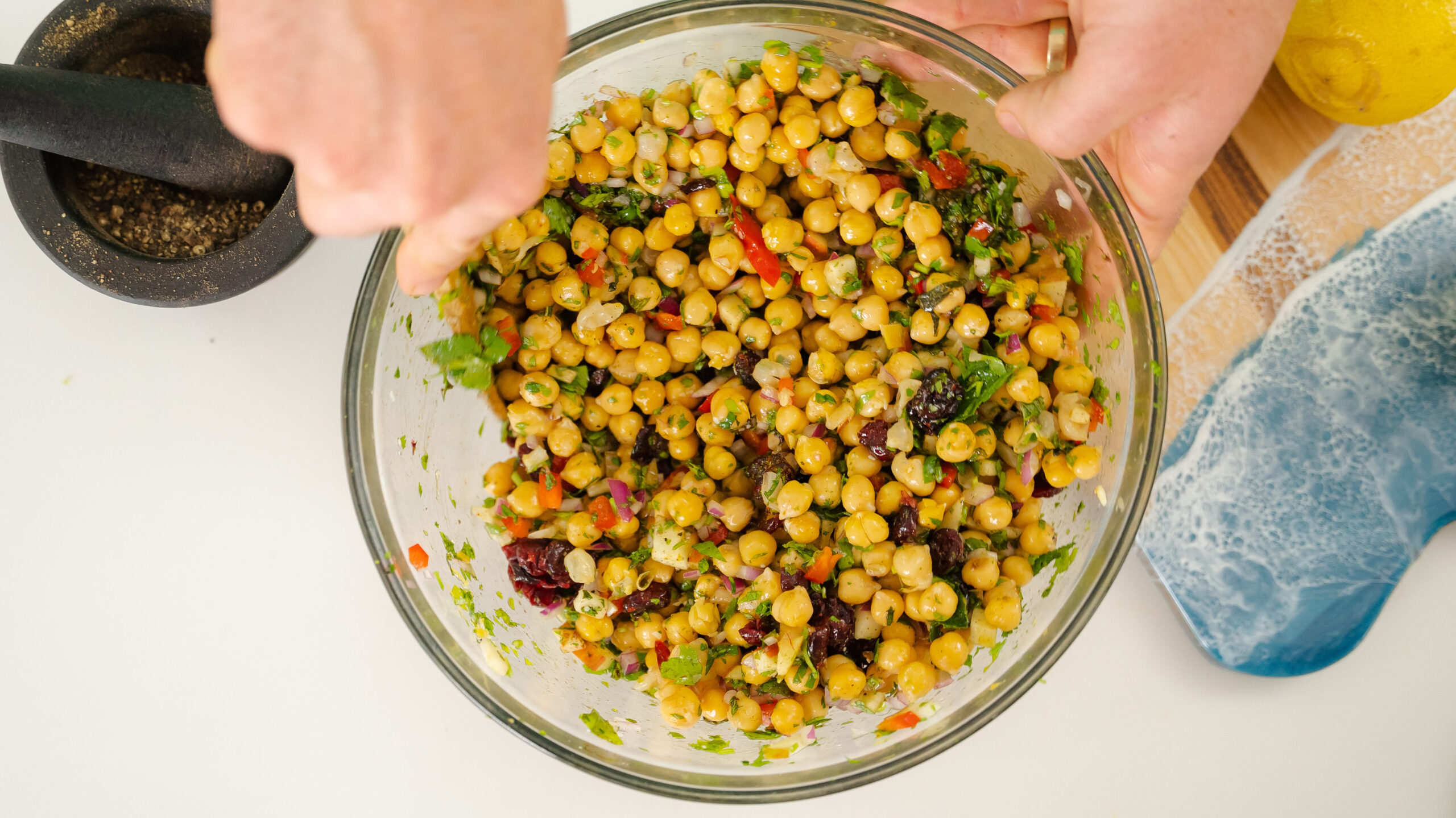 A chickpea salad in a large clear bowl being stirred with a spoon.