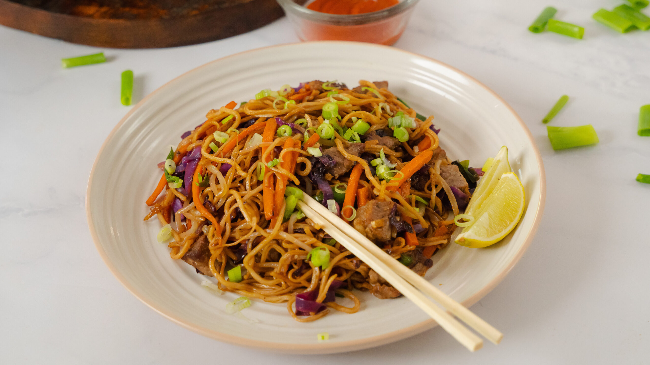 Asian beef noodles with ginger being scooped up with chop sticks on the side.