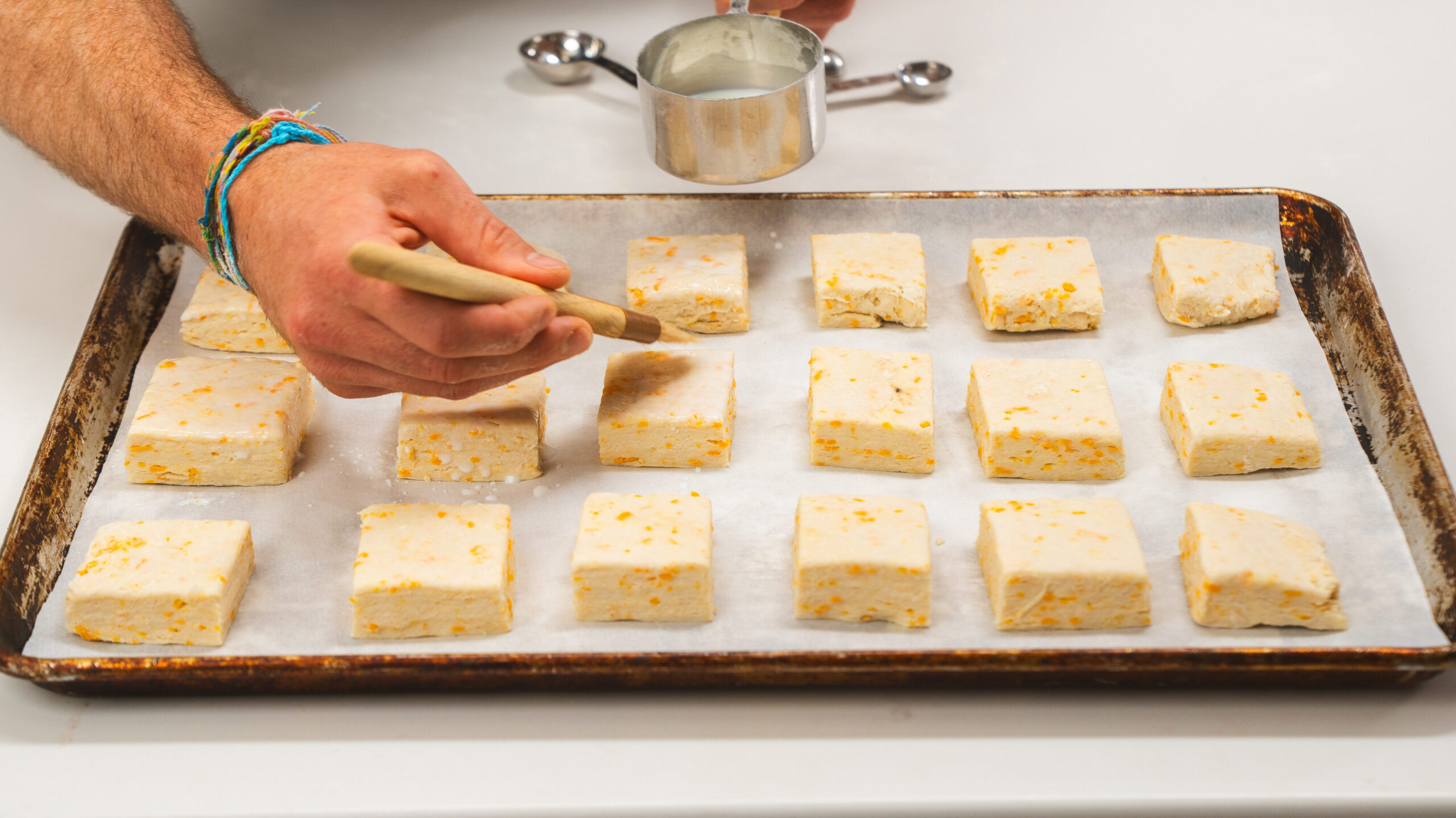 Buttermilk biscuits on a parchment lined baking sheet being brushed with buttermilk.