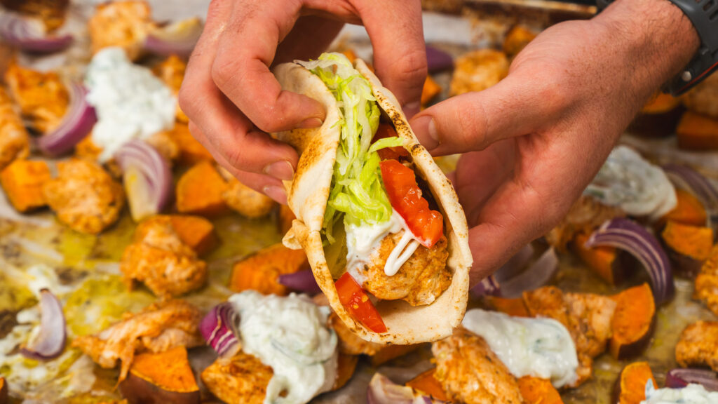 Sheet pan chicken shawarma in a pita loaded with lettuce, tomato and yogurt sauce.