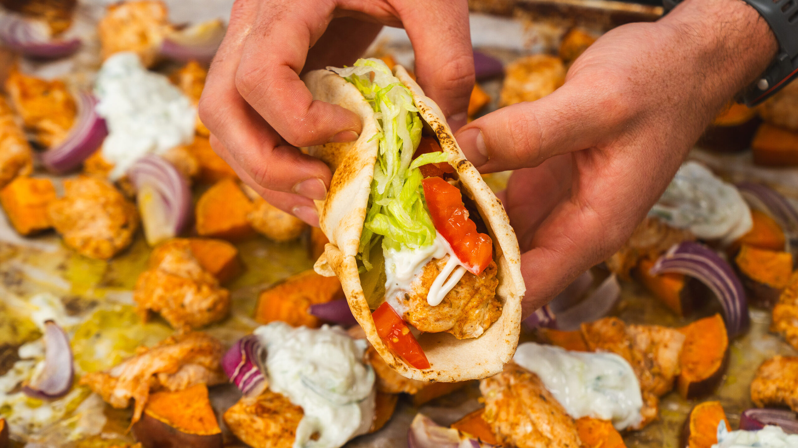 Sheet pan chicken shawarma in a pita loaded with lettuce, tomato and yogurt sauce.