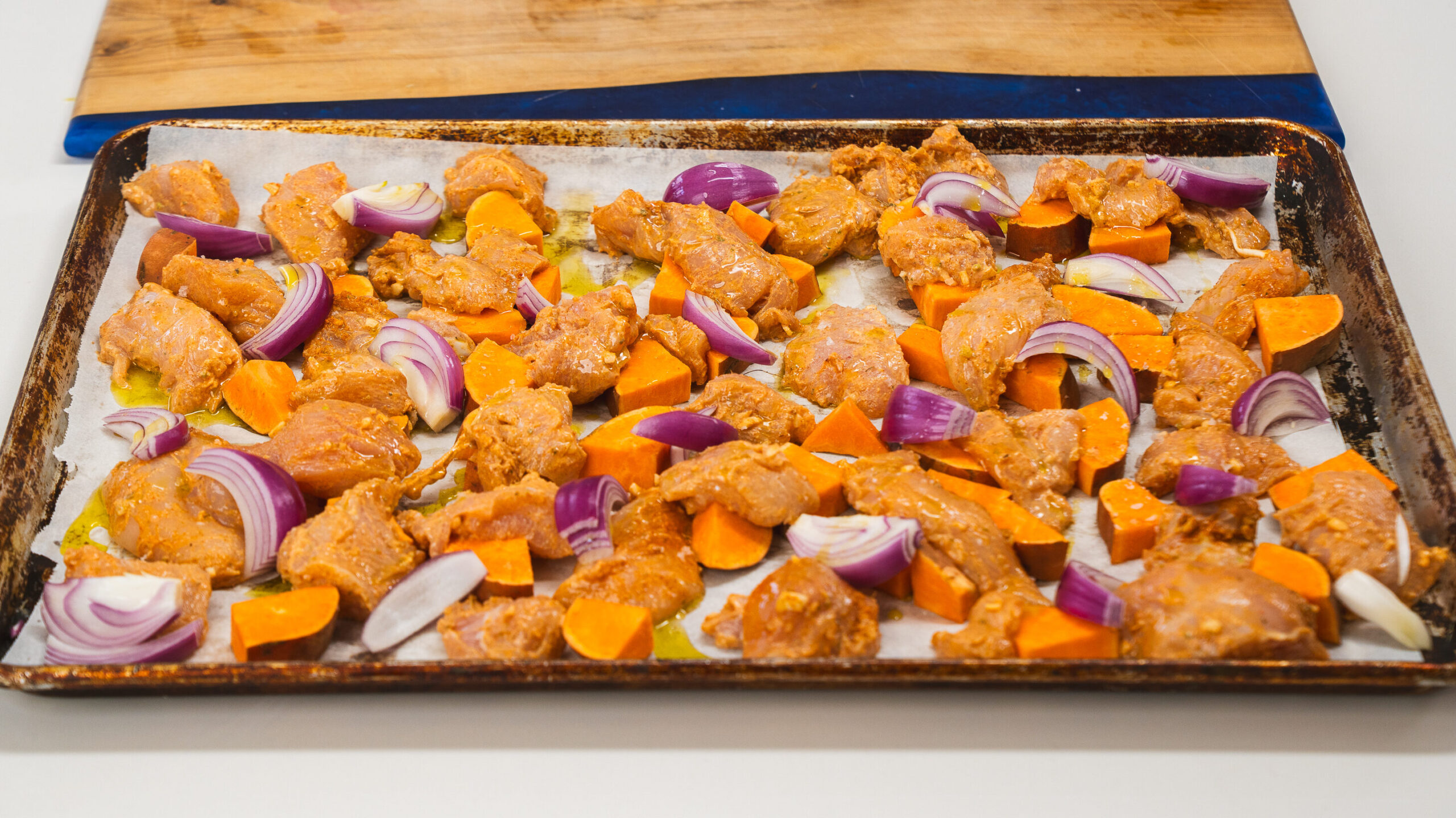 Sheet pan chicken shawm on a baking sheet wth red onion and sweet potatoes.