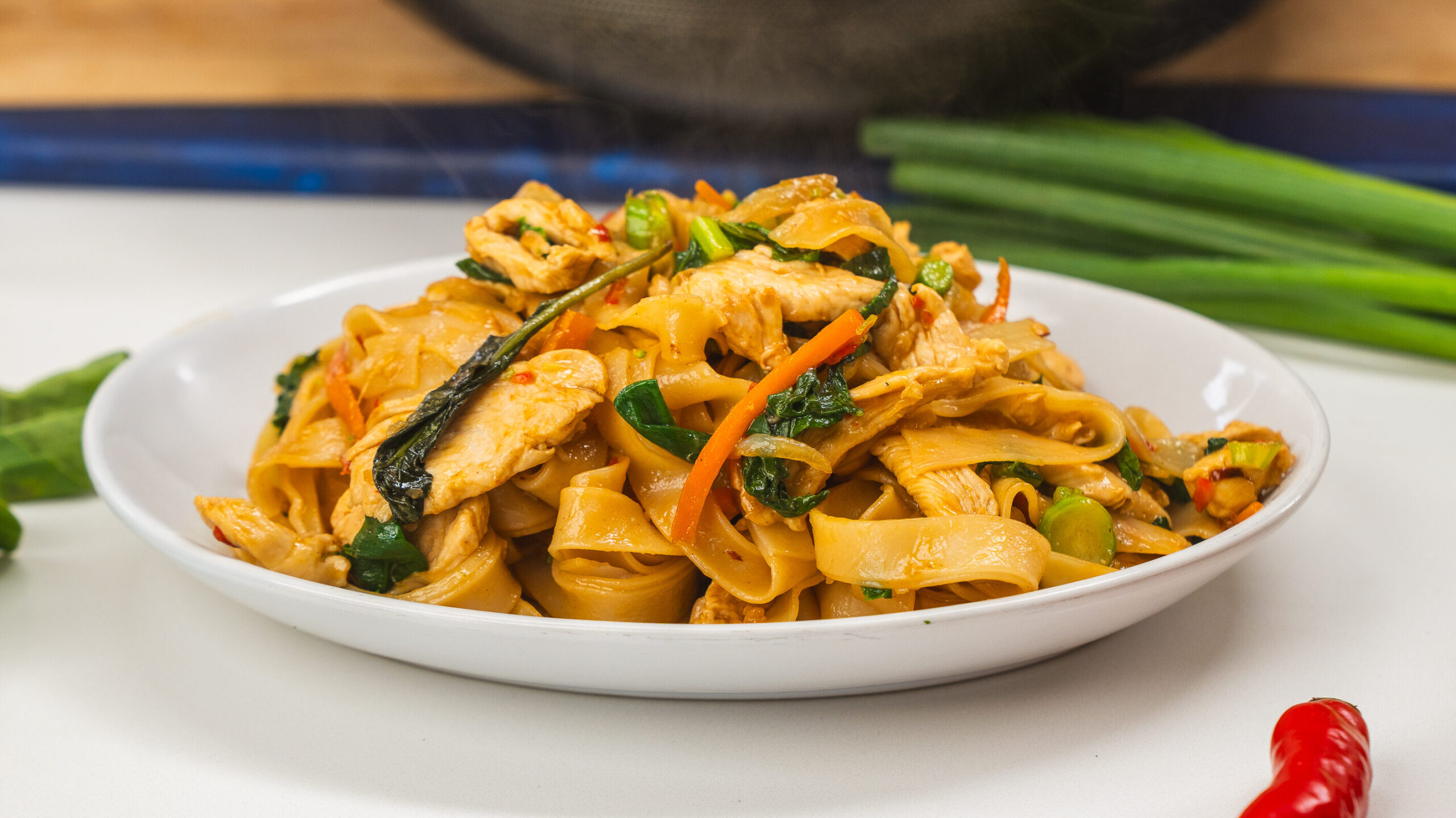 Thai drunken noodles on a white plate with fresh vegetables.