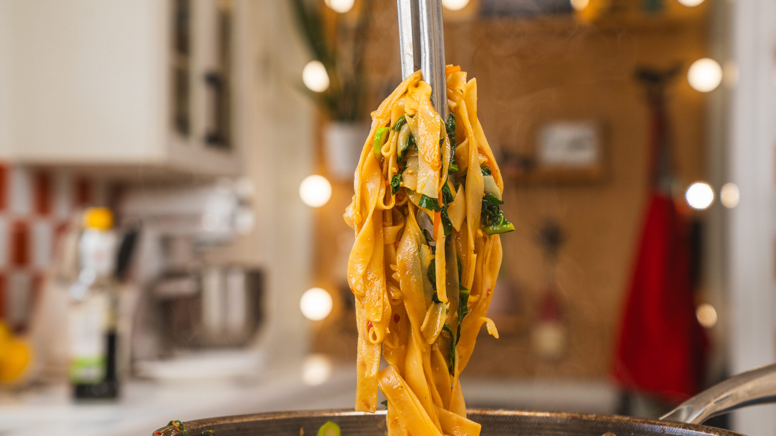 Thai drunken noodles being held up with tongs.