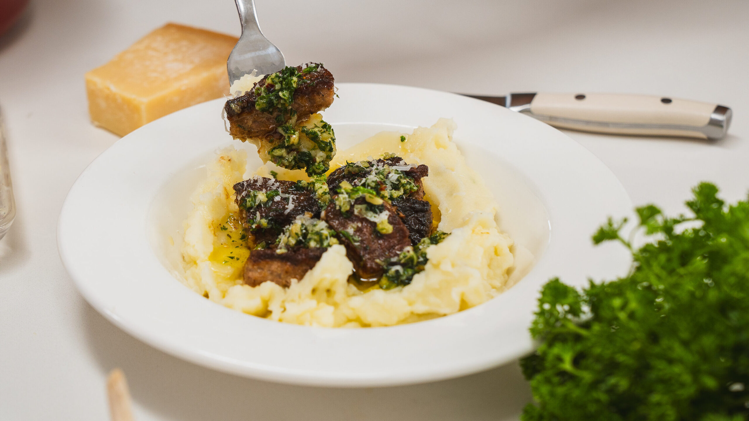 Garlic. butter steak bites in a white bowl served over mashed potatoes.