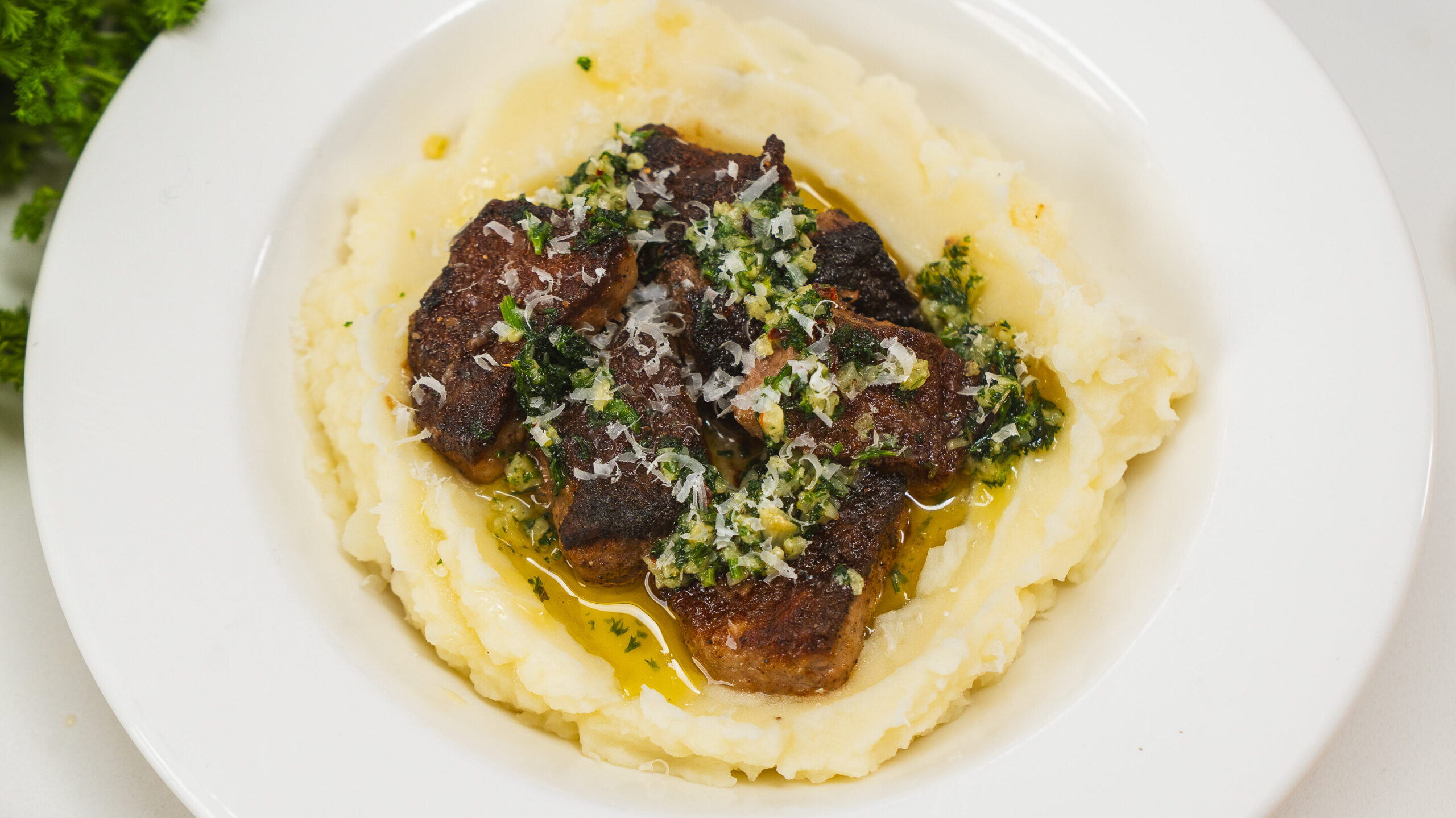 Garlic butter steak bites served over mashed potatoes in a white bowl.