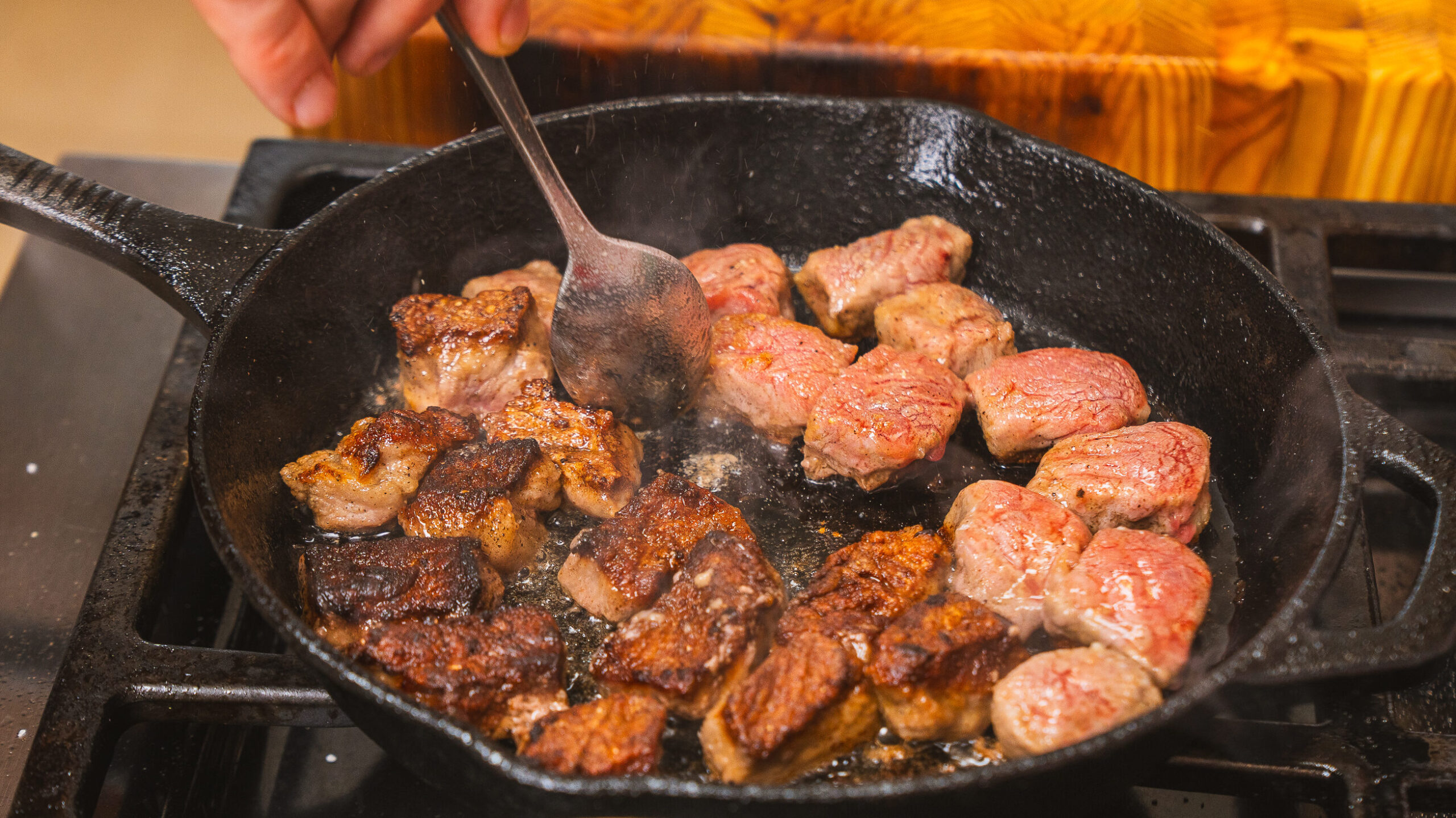 Steak bites being seared in a. cast iron pan.