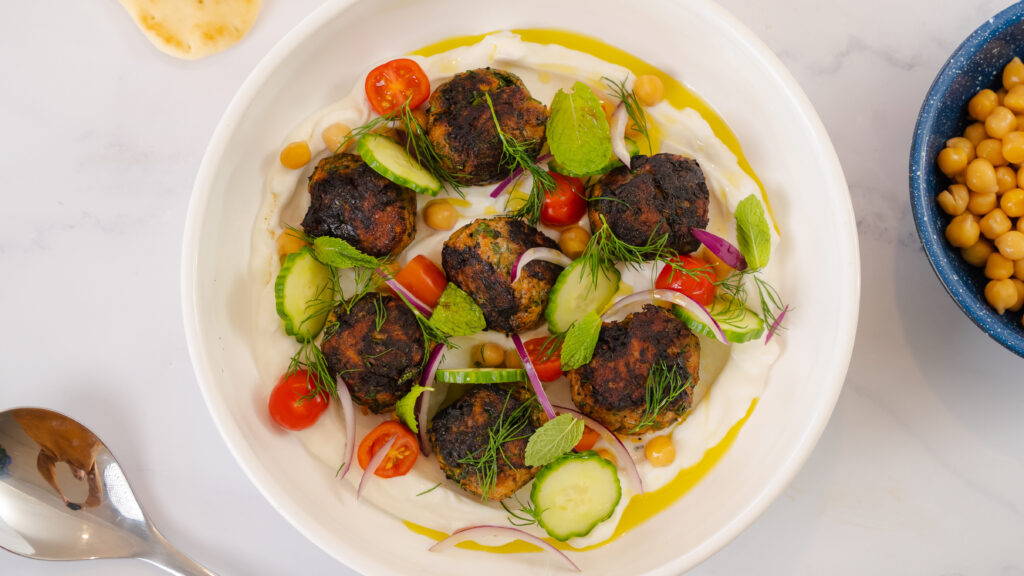 Harissa chicken meatballs on a white plate over yogurt and herbs.
