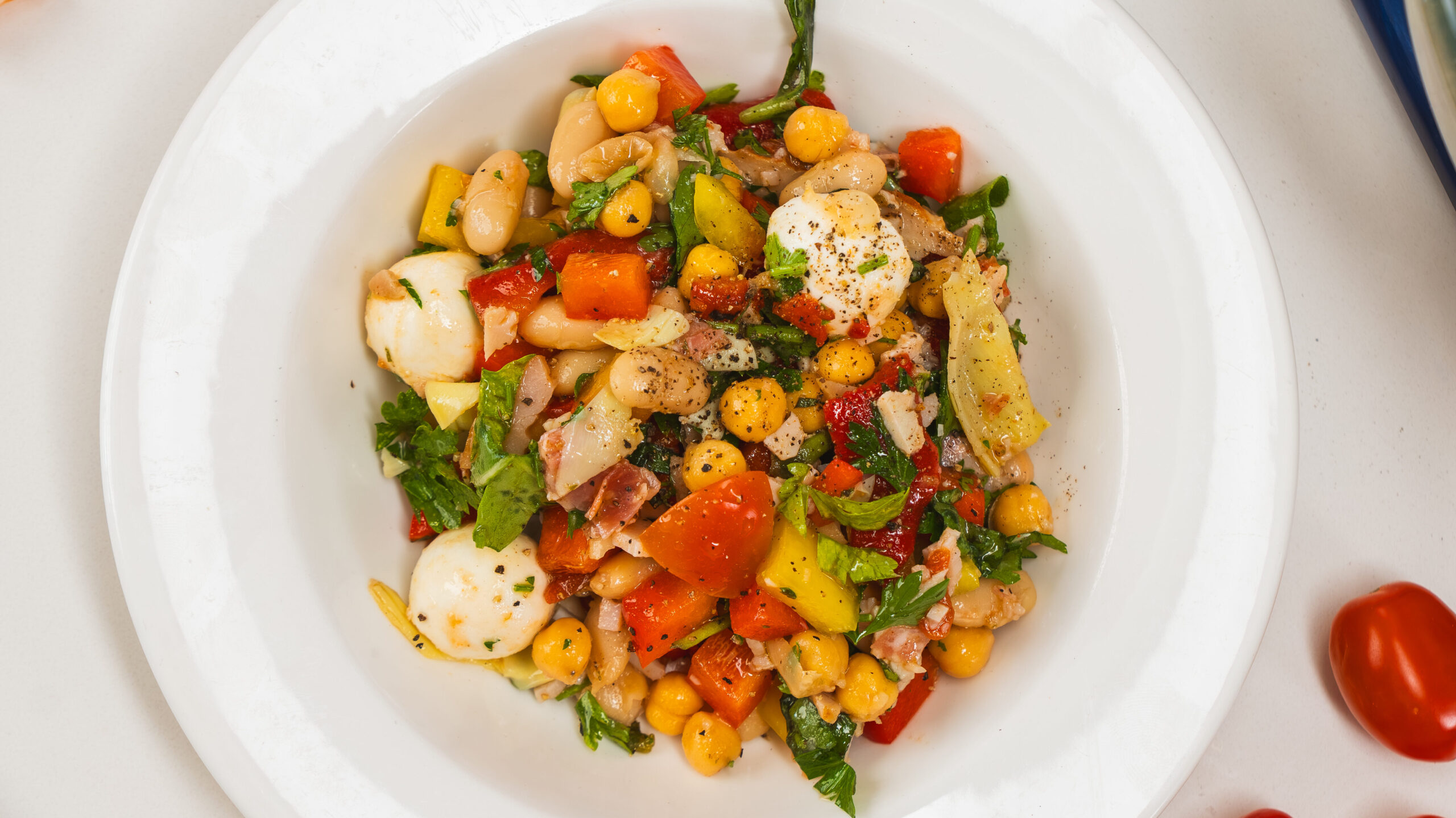 Dense chopped bean salad in a white bowl with scattered cherry tomatoes to the side.