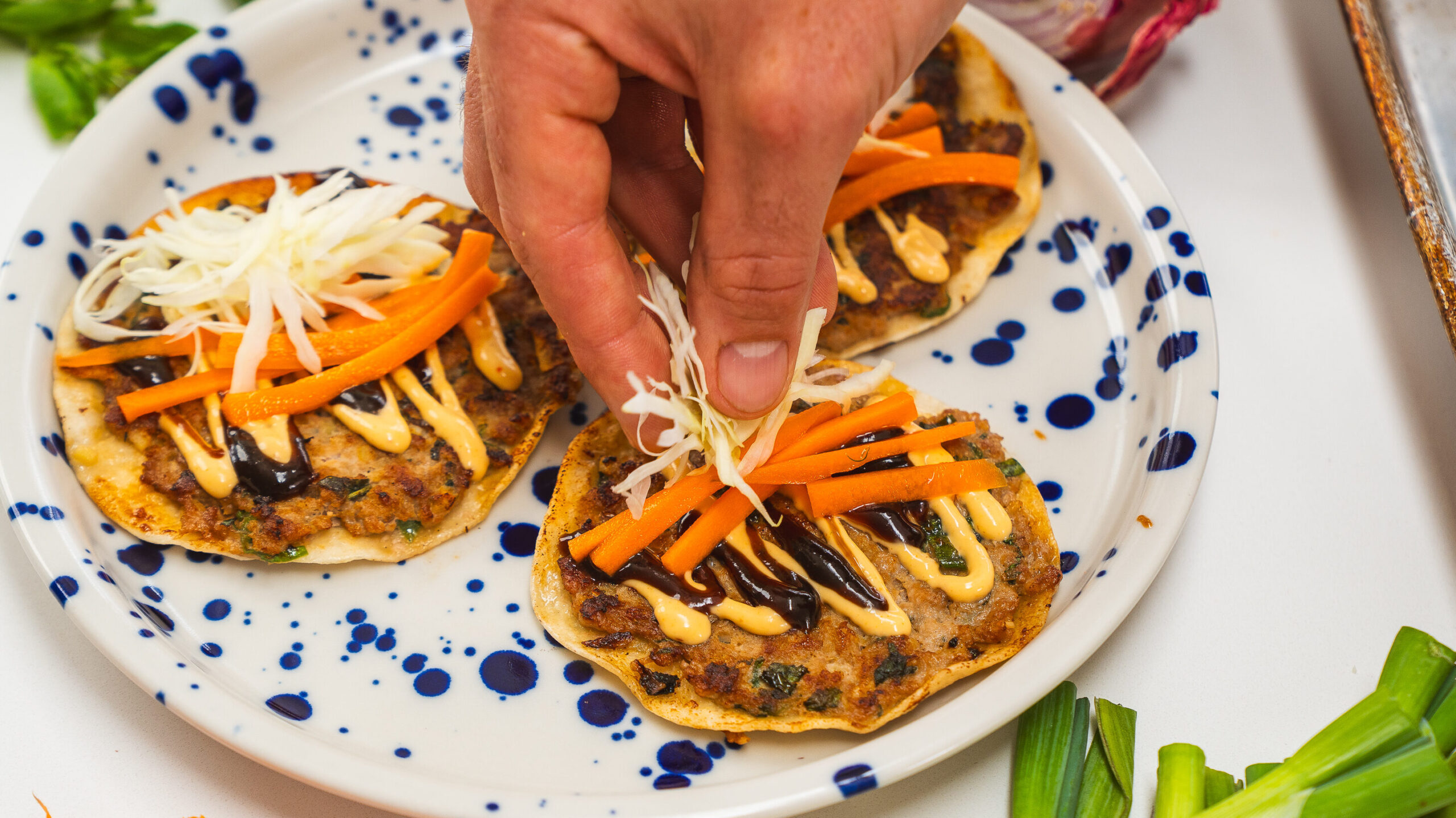 Toppings being assed to smash dumpling tacos.