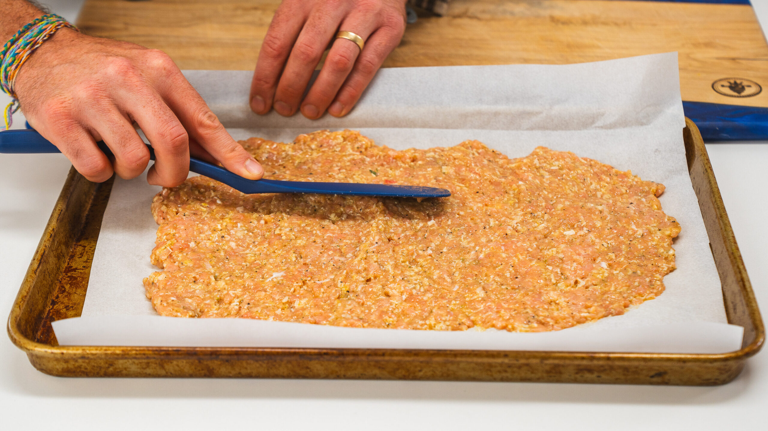 Chicken crust pizza being spread on a baking sheet with a spatula.