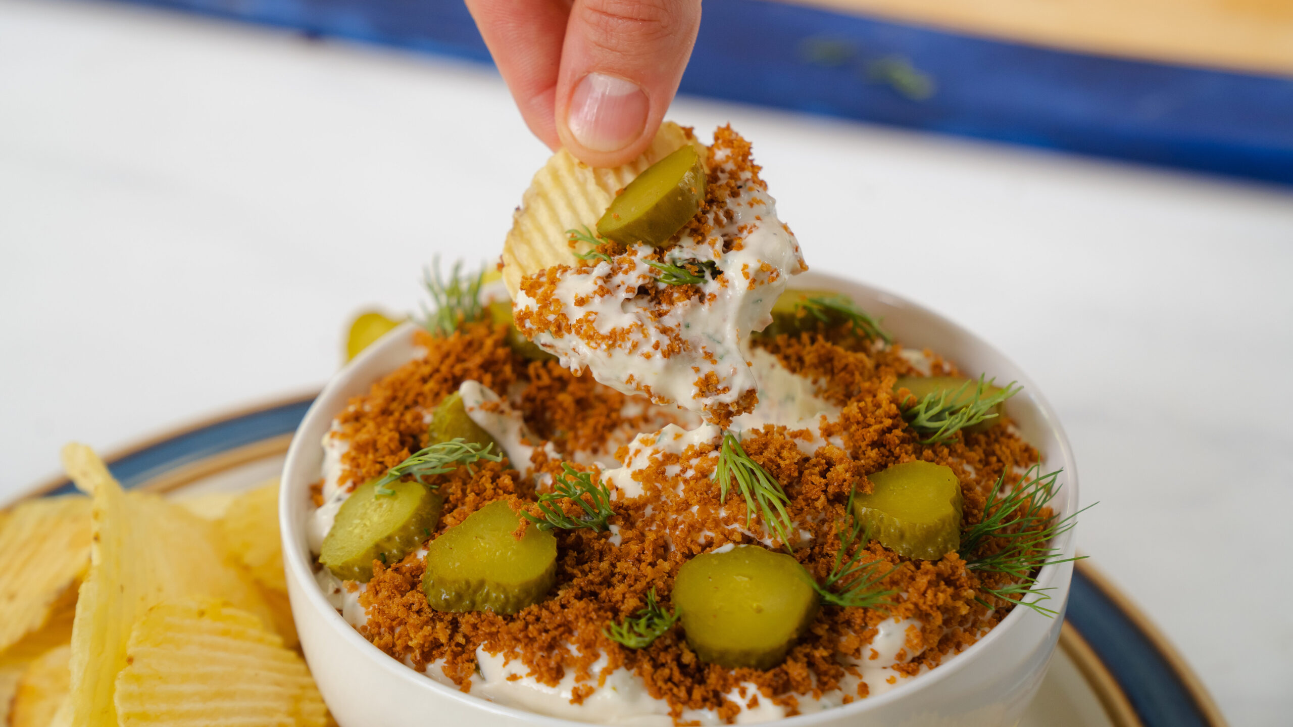 Someone taking a dip into this dill pickle dip with a ruffled potato chip.