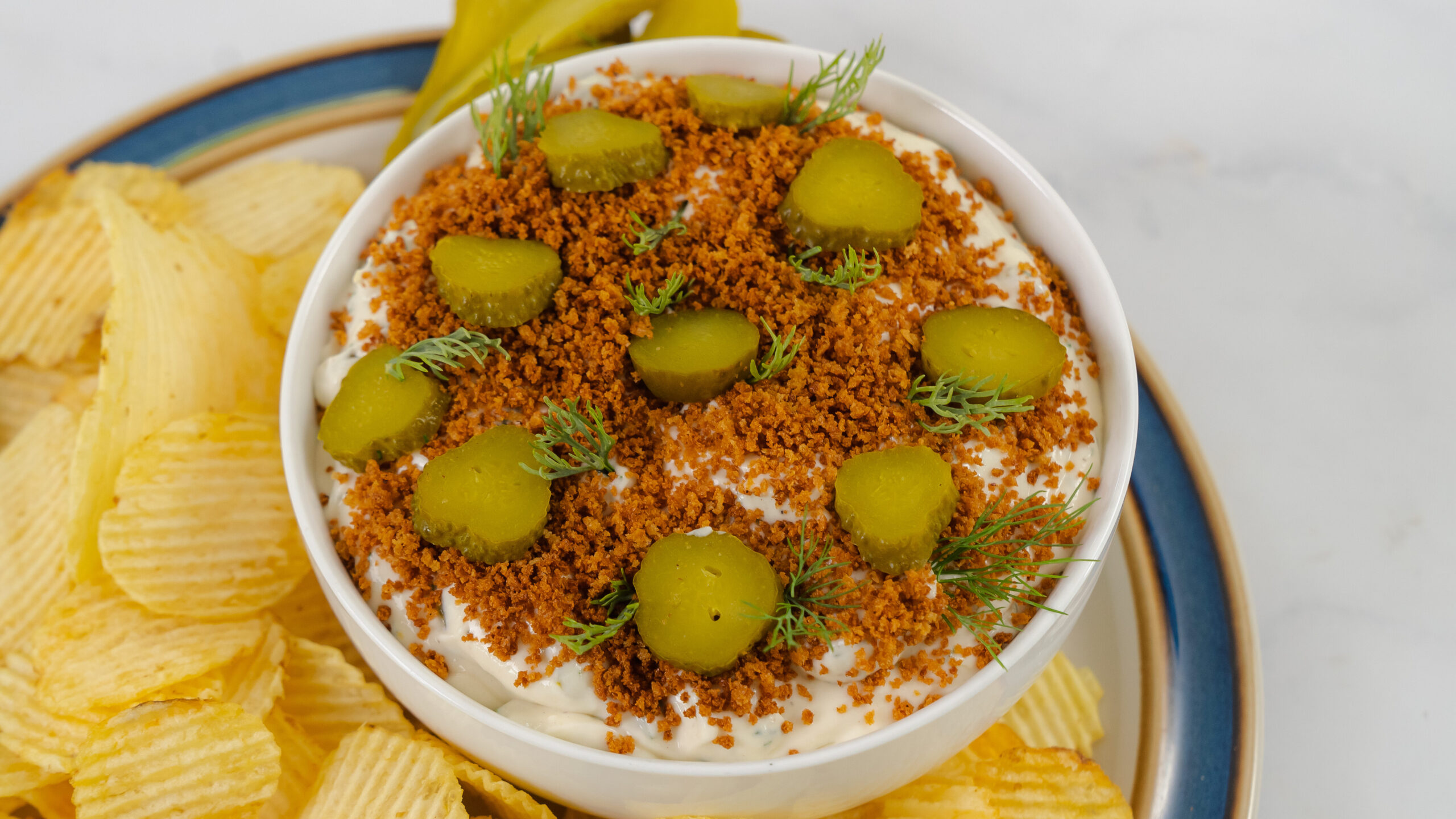 Dill pickle dip in a bowl, surrounded by ruffled potato chips.