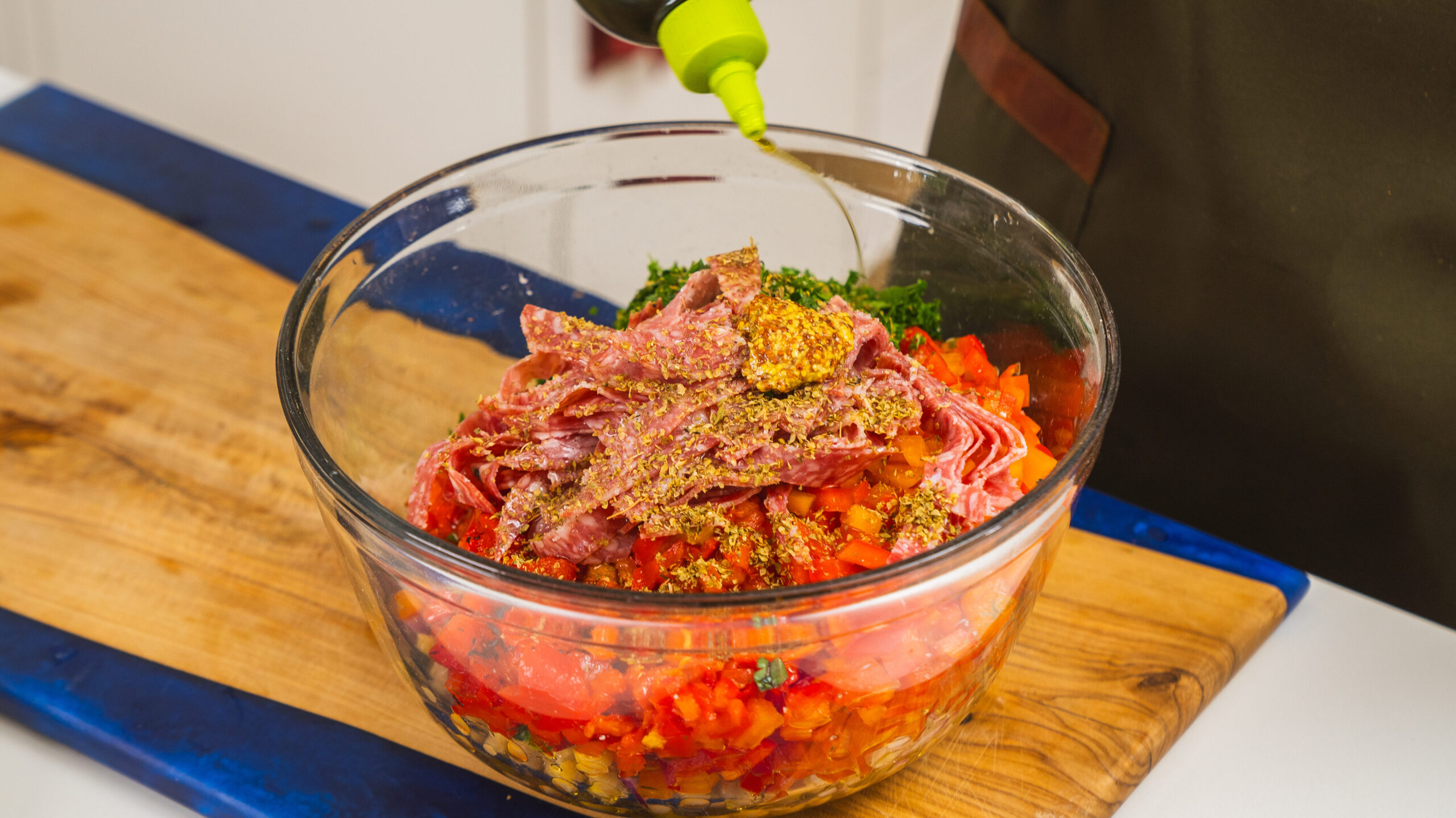 La Scala salad ingredients in a large mixing bowl with olive oil being poured in.