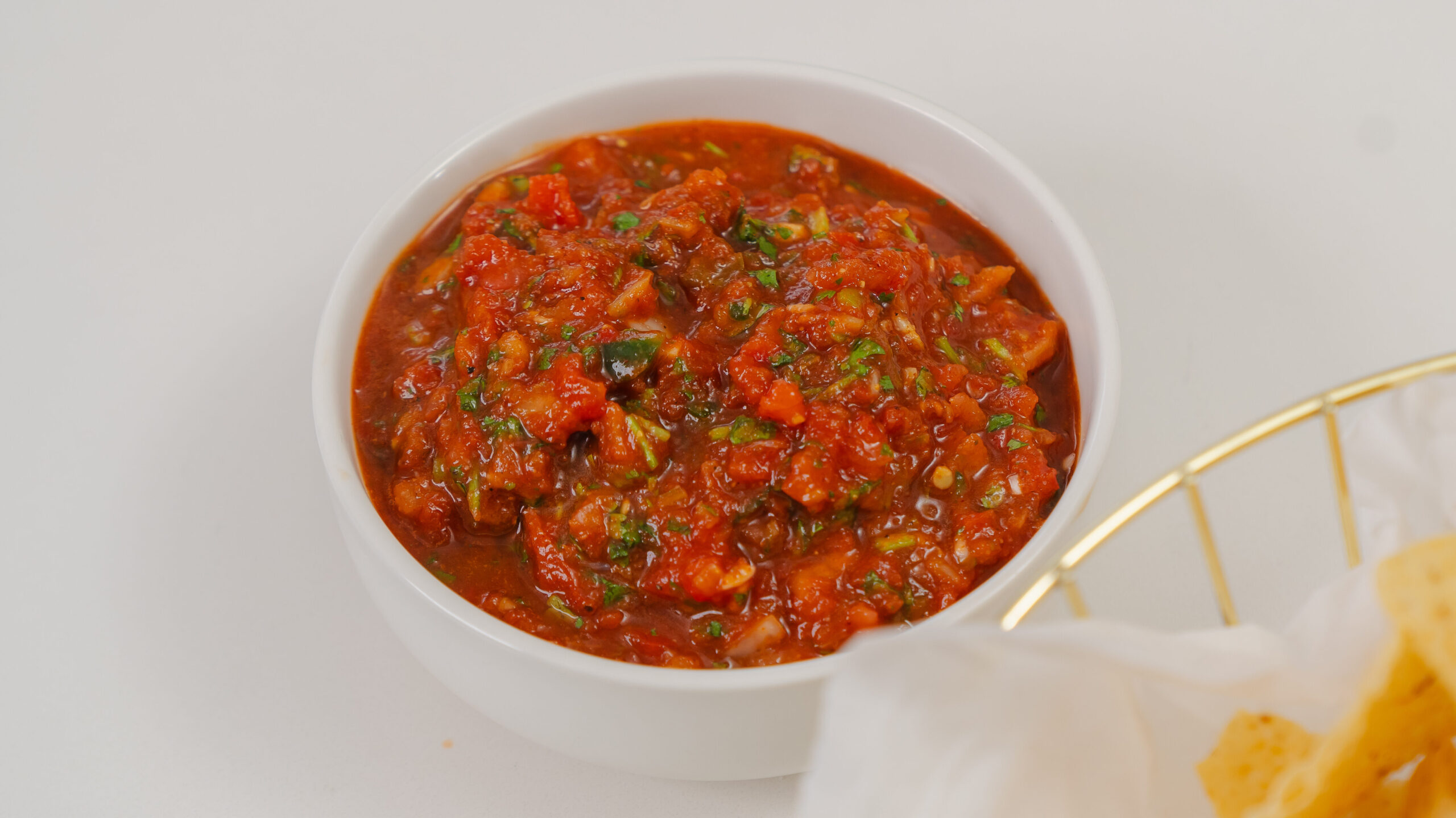 Homemade salsa in a white bowl with nacho chips nearby.